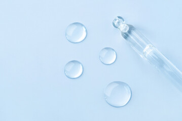 Drop of cosmetics and a pipette on a blue background. A product for skin, face or hair care.