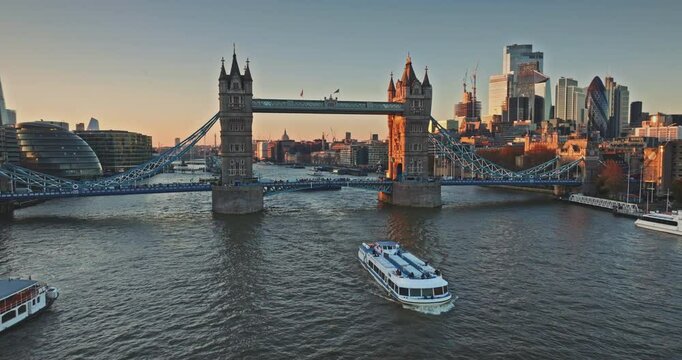 Aerial view of Tower Bridge, one of London's most famous landmarks, City Hall, River Thames and skyscrapers of City of London in background at sunset. Tourist excursion boat. Drone flight footage