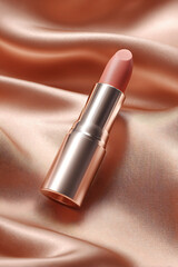 Obraz premium Elegant nude lipstick showcased on a luxurious peach satin background, perfect for beauty or fashion advertising.