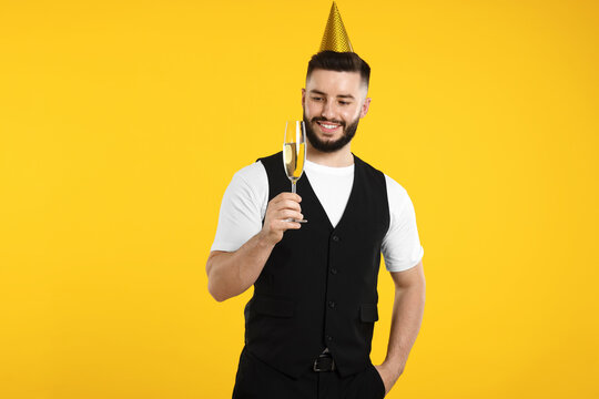 Happy Birthday. Handsome man with party hat and glass of champagne on orange background - Powered by Adobe