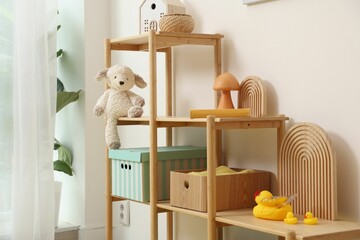 Shelving unit with decor and toys near white wall in stylish playroom. Interior design