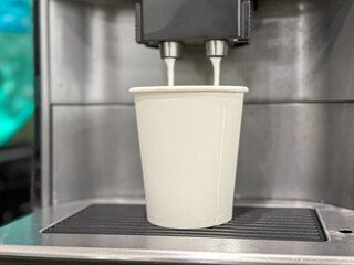 Milk is whipped for cappuccino. Making coffee by coffee machine into paper cup, latte coffee coming out from an automated coffemaker machine. Beverage drink for breakfast. Vending machine. 