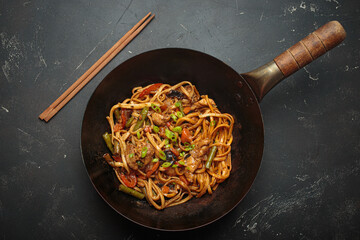 Wok pan with stir fry chicken and vegetable noodles, with wooden chopsticks resting on top, top...