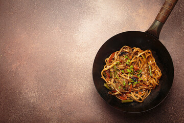 Wok pan with stir fry chicken and vegetable noodles, with wooden chopsticks resting on top, top...