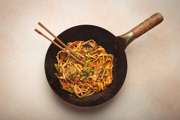 Wok pan with stir fry chicken and vegetable noodles, with wooden chopsticks resting on top, top...