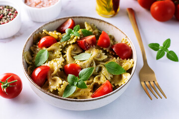 Aromatic homemade vegan farfalle with green pesto sauce, cherry tomatoes, basil leaves and homemade spicy olive oil close up. Healthy vegan food concept.