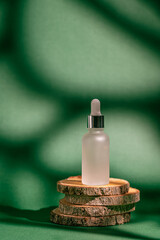 A frosted dropper bottle of facial serum stands on a wood stand against a green background, perfect...