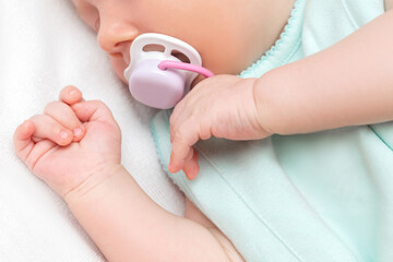 Cute little newborn infant baby with nipple sleeping lying on bed sheet.Close up of child hands...