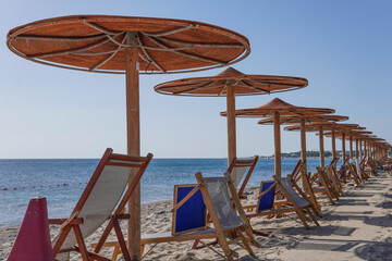 A bay on the southern coast of Italy with clear blue sea, mountains in the background and a sandy beach surrounded by colorful umbrellas and sun loungers.