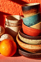 Ceramic cups and plates stacked artistically on an orange surface, showcasing rich textures