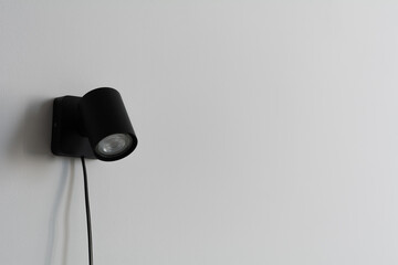 Modern black wall-mounted spotlight with adjustable head on a minimalist gray wall.