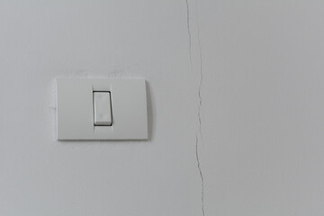 White plastic switch on a white wall. To the right of the switch there is a crack along the height of the wall.