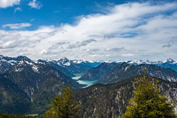 A breathtaking view of alpine mountains with snow-capped peaks and a turquoise lake in the valley, under a dynamic cloudy sky, perfect for hiking, travel, outdoor and nature themes