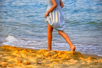 A girl runs along the sea at sunset, lifting her dress slightly.