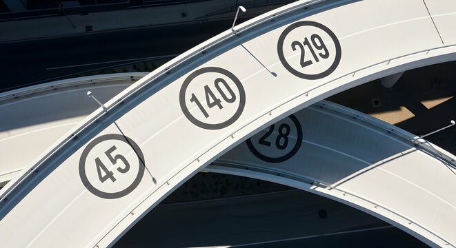 Aerial view of a modern highway interchange with abstract numeric signage indicating distance or identifiers on curving overpasses
