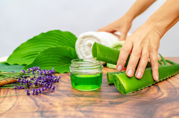 Female hands holding aloe vera leaf above bottle with gel. Aloe vera, towel, lavender. Advertising.
