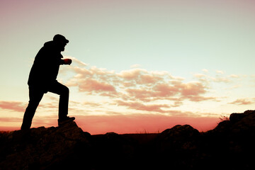 The silhouette of a Man climbs a cliff