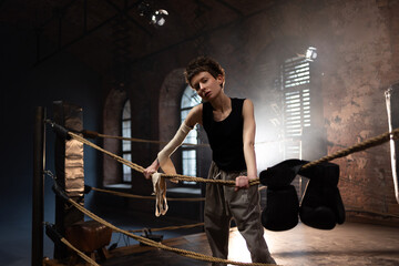 Boxer woman with short hair pausing on ropes, cinematic gym training atmosphere
