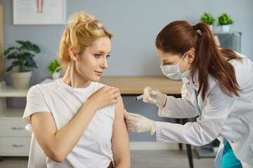 Vaccine injection into arm of young woman patient in hospital. Nurse in gloves holding needle of...