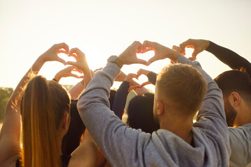 Friends group making heart shape gesture with fingers in sunlight. Happy people raise hands to sun...