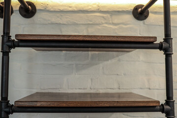 Close-up of dark wood industrial shelf on black metal pipe frame mounted to white brick wall,...
