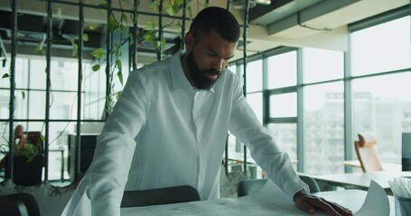 A professional in a modern office is meticulously analyzing various project plans for effectiveness - Powered by Adobe