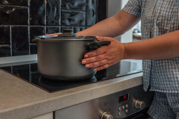 Person placing a metal pot on an induction stove in a modern kitchen with black tile backsplash and...