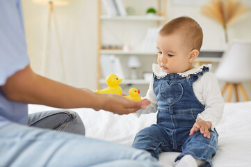 Newborn baby and mother play with yellow ducks, child looking with curiosity at new toys. Mom and...