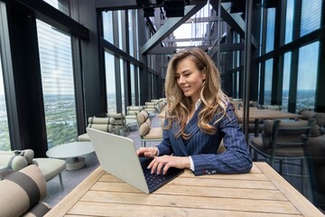 A professional woman works on her laptop in a sleek office with city skyline views, highlighting...
