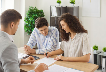 Cheerful Caucasian couple signing a contract reaching agreement with a man realtor or financial...
