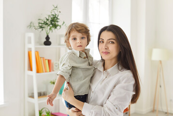 Portrait of a happy mother holding son at home living room, showcasing family affection and...