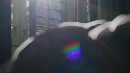 Colorful rainbow flare falling on blanket as sunlight enters bedroom through open window, dust particles floating in calm and quiet early morning space