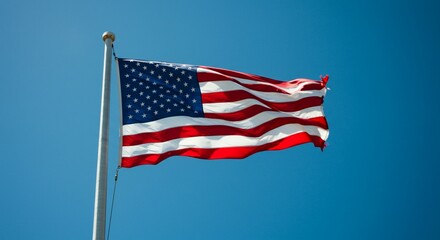 Obraz premium The American flag waves proudly against a clear, vibrant blue sky, representing national pride.