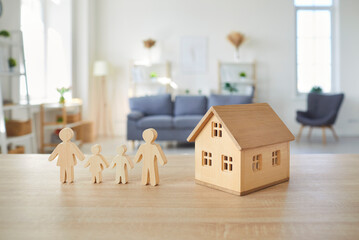 Close up photo of wooden figures of father, mother and two children and toy house standing at table...