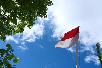 Indonesian flag swaying in the wind against blue sky and trees. Flag of Indonesia. Independence day celebration concept, patriotism concept. Embassies and consulates of countries