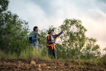 Two people are standing in a forest, one of them pointing at something. They are both wearing backpacks