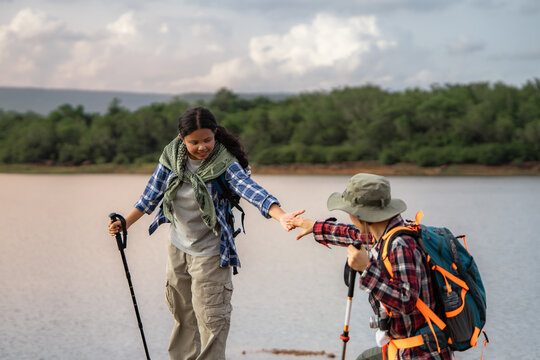 A woman is helping a man cross a river. They are both wearing backpacks