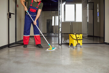 Cropped shot of janitor cleaning floor with mop inside modern commercial building. Cleaning crew member in uniform maintaining cleanliness and hygiene in office space. Routine cleaning service.