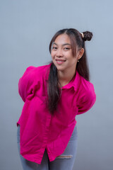 Smiling Indonesian Asian woman wearing a bright pink shirt and ripped jeans, leaning forward with...