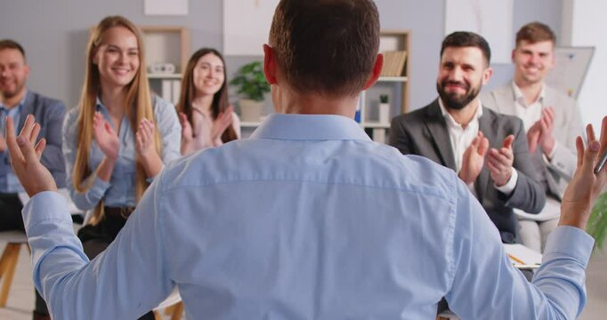 Happy office workers congratulating his man colleague with promotion, making applauds. Businessman giving report or presentation to group of people, telling about project strategies