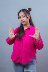 Asian Indonesian woman in a pink shirt showing both hands raised in a stop gesture. She looks...