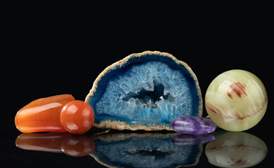 Polished natural minerals on a black mirror background. Carnelian (chalcedony variety), agate geode with quartz crystals, amethyst, polished onyx sphere.