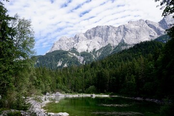 Grüner Bergsee vor felsigem Alpenmassiv unter wolkigem Sommerhimmel