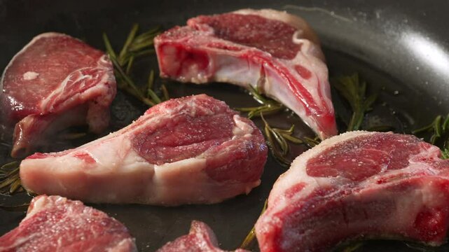 Raw lamb chops seasoned and arranged on pan with sprigs of rosemary before cooking, showing detailed texture and marbling of fresh uncooked meat