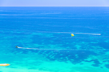 Parasailing in sea, motorboat powerboat with attached parachute on azure turquoise water of Mediterranean Sea, water sport on summer vacation, motor boat раrasailing, Alicante bay aerial view, Spain