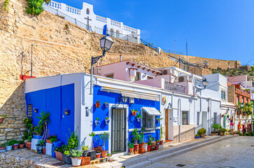 Alicante old town Santa Cruz with narrow street, typical white houses with flowers and plants and Ermita de la Santa Creu d'Alacant church in Alicante city historic centre, Valencian Community, Spain