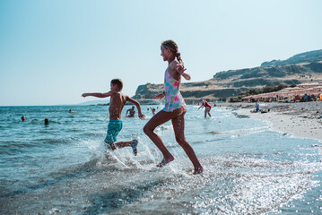 Siblings running into water during summer beach holiday.
