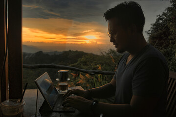 Man Working on Laptop Outdoors at Sunset with Mountains in Background