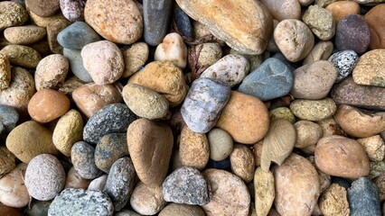 A close-up image of various smooth river pebbles in different colors and textures. The stones are...