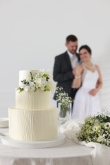 Happy married couple together indoors, focus on wedding cake and bouquet on table